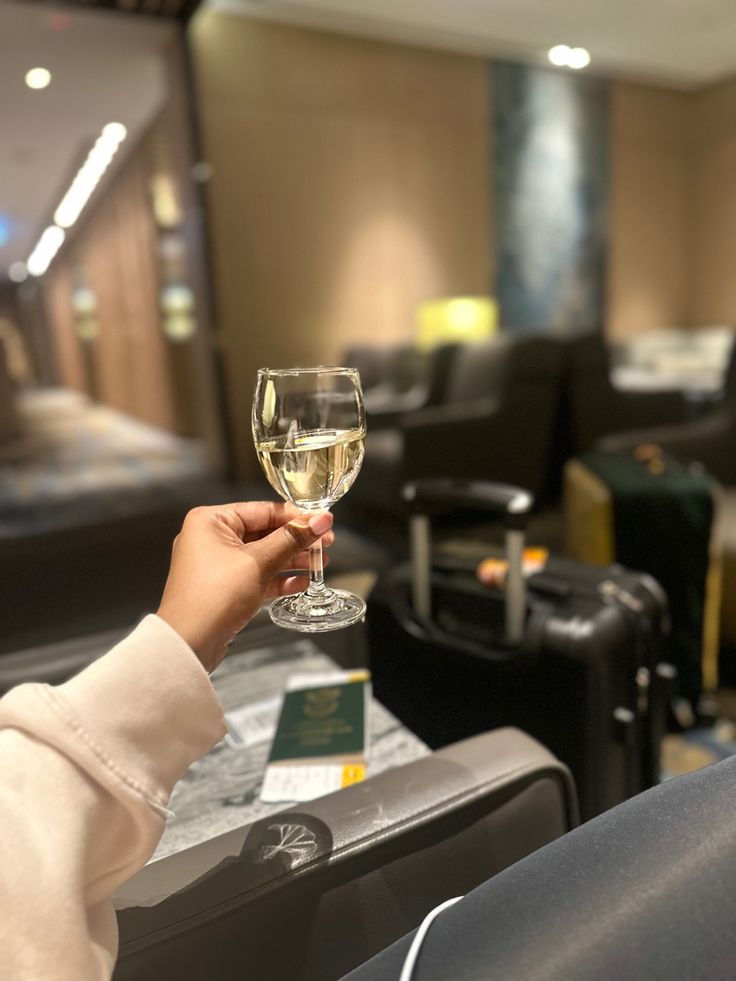 a person holding a glass of wine in front of luggage at an airport lounge area