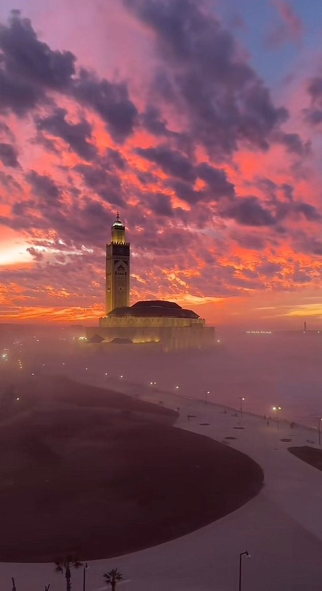 a clock tower in the middle of a foggy city at sunset with lights on