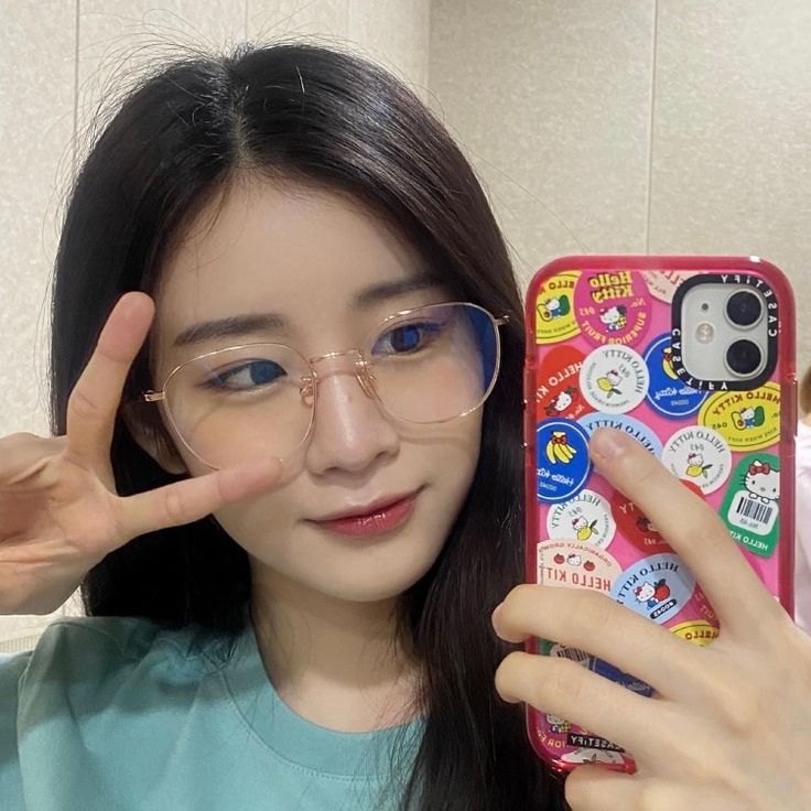 a girl with glasses is holding up her cell phone to show the peace sign and making a hand gesture