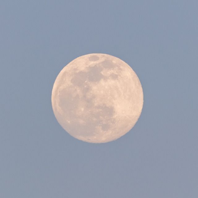 an airplane flying in front of a full moon on a clear blue sky with no clouds