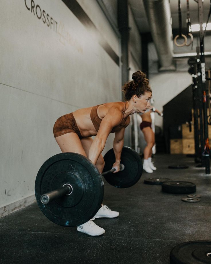 two women doing squats with barbells in a crossfit gym area