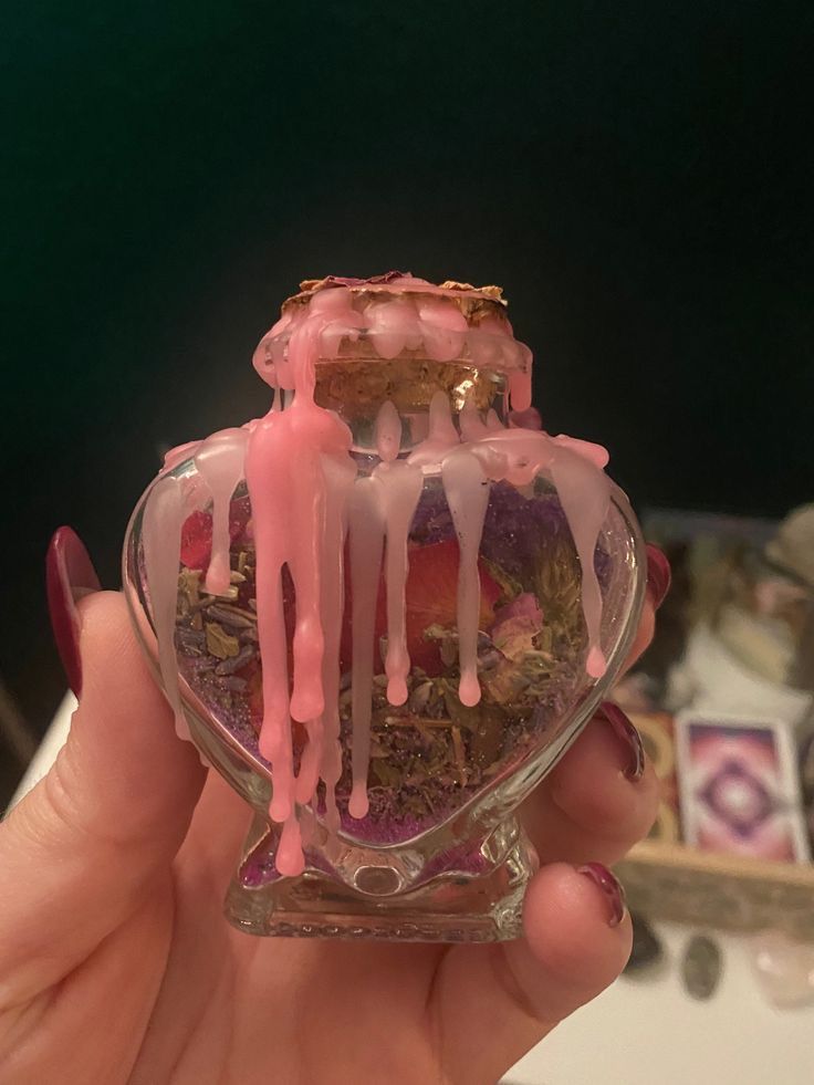 a hand holding a small glass vase filled with flowers and ice cream on top of it