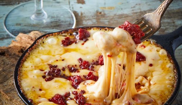 a person is eating food in a skillet with cheese and cranberry sauce