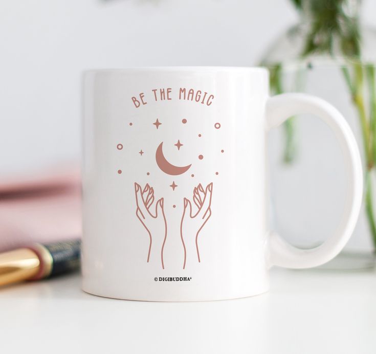 a white coffee mug with the words be the magic written on it and two hands holding stars