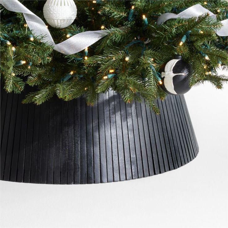 a christmas tree in a black pot with white ribbon and ornaments on it's top