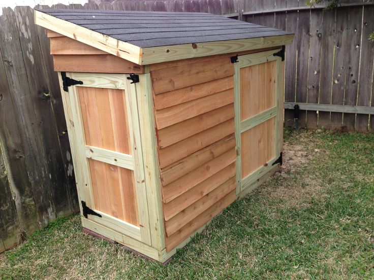 a wooden shed sitting in the grass next to a fence