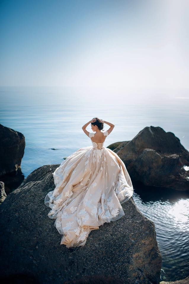 a woman standing on top of a rock next to the ocean wearing a wedding dress