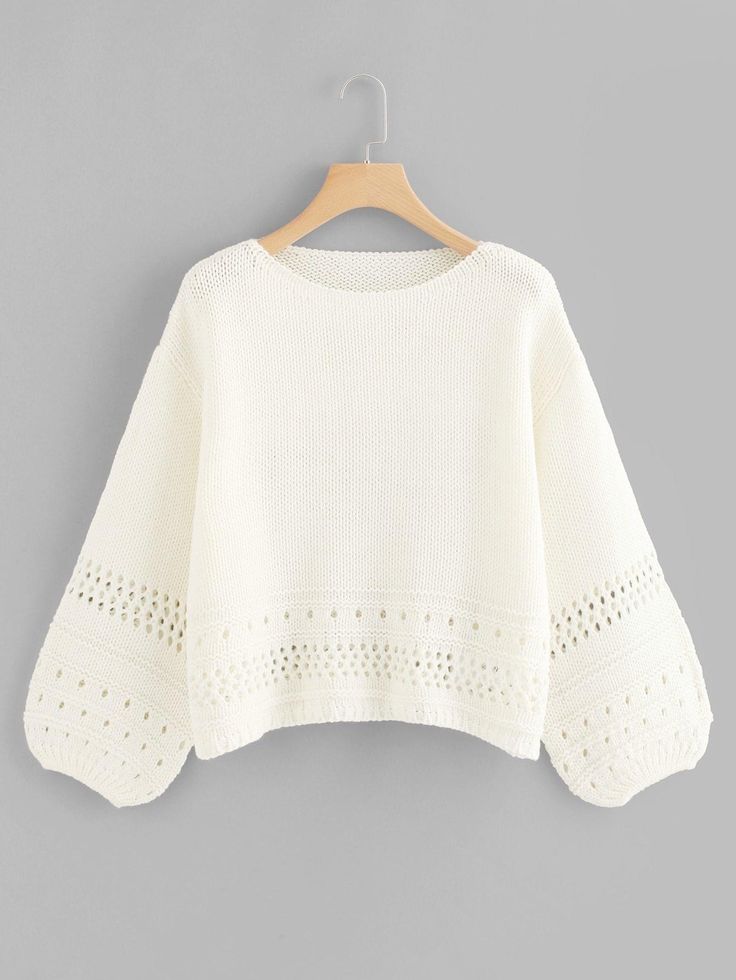 a white sweater hanging on a hanger with an openwork design and cut outs