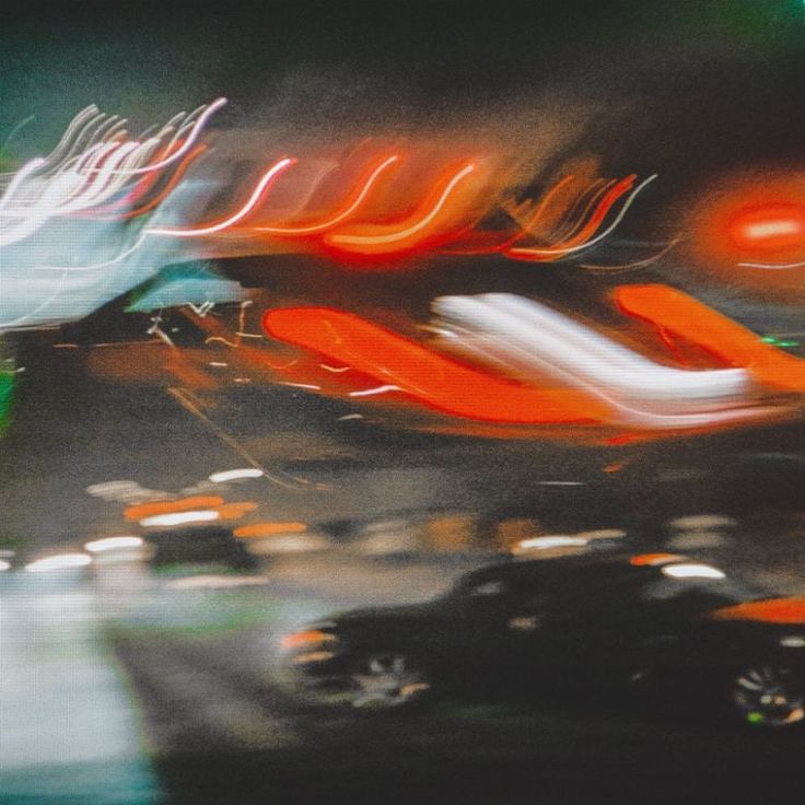 blurry photograph of cars driving down the road at night time with neon lights in the background