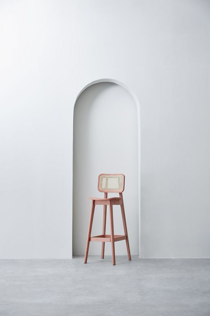 a pink chair sitting in front of a white wall with an arch on the side