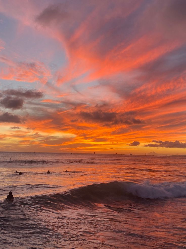 surfers are riding the waves at sunset on their surfboards in the ocean with colorful clouds