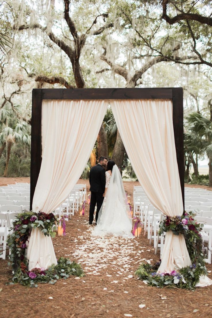 a bride and groom standing under an outdoor wedding ceremony arch with white draping