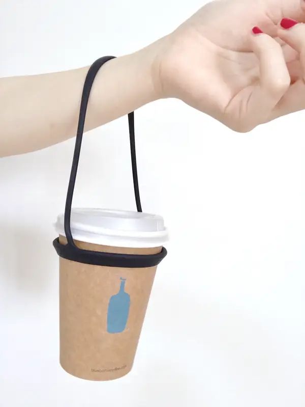 a woman's hand holding a coffee cup with the lid open and a black string attached to it