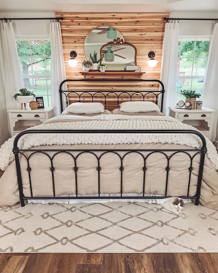 a bedroom with a metal bed frame and white pillows on top of it, along with two windows