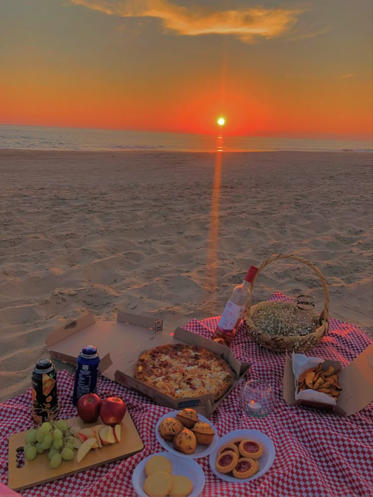 a picnic on the beach at sunset with pizza, fruit and snacks in front of it