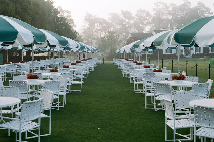 tables and chairs are lined up under umbrellas on the grass in an open field