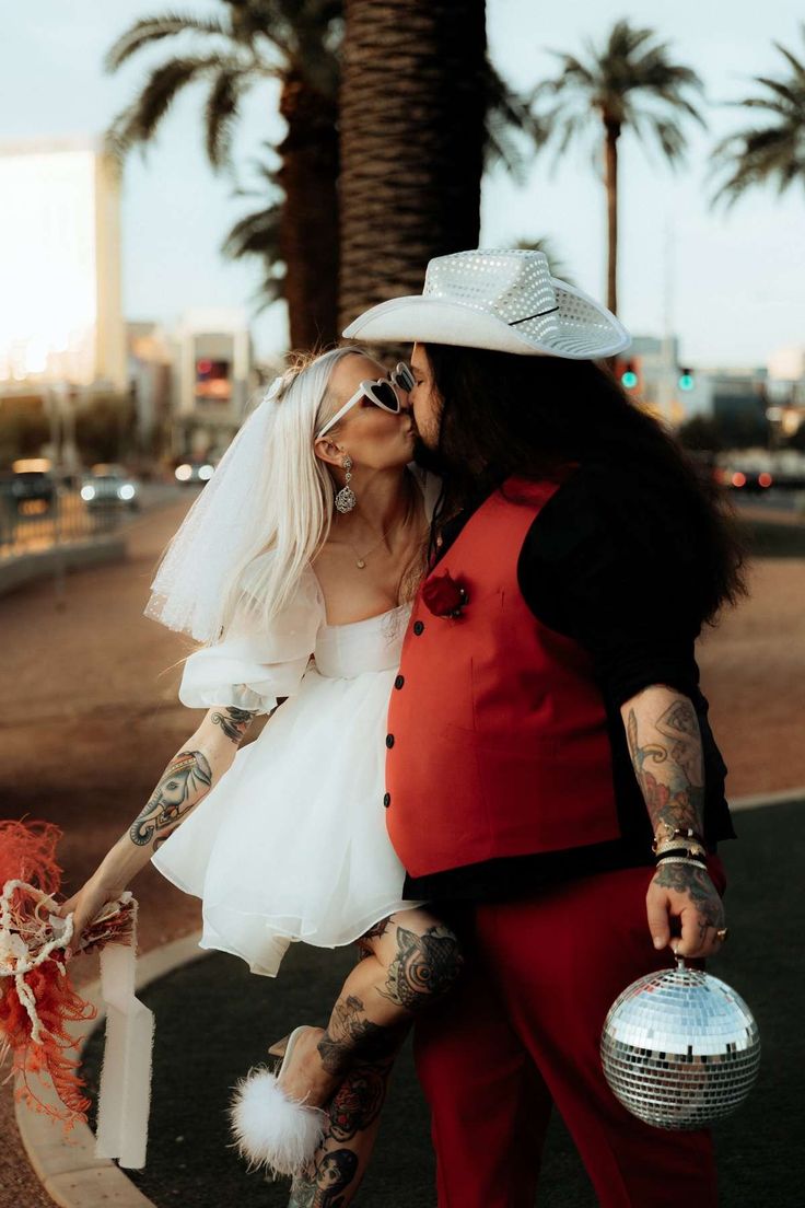 a man and woman dressed in costumes kissing each other on the street with palm trees behind them