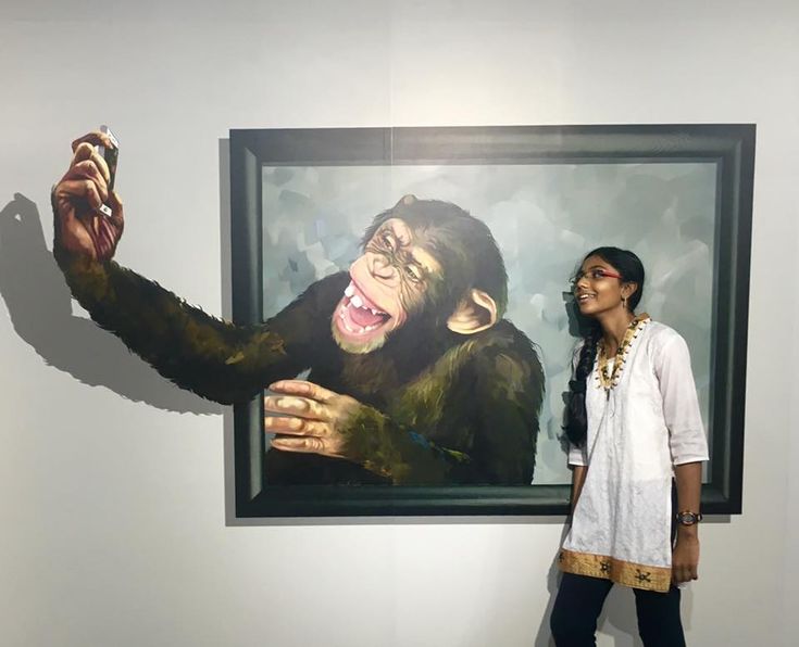 a woman standing in front of a painting of a chimpan holding something up to her face