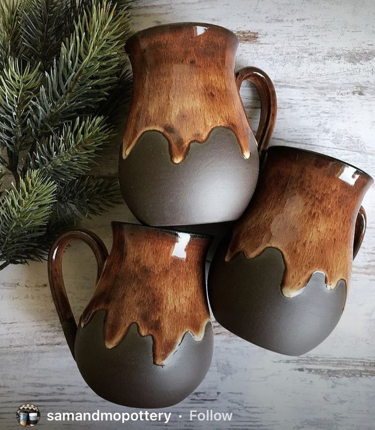 three brown vases sitting on top of a wooden table next to a pine tree