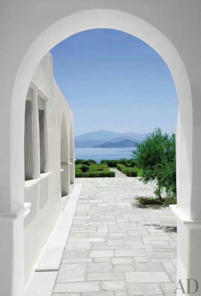 an archway leading to the ocean with white walls and stone flooring, along with greenery on either side