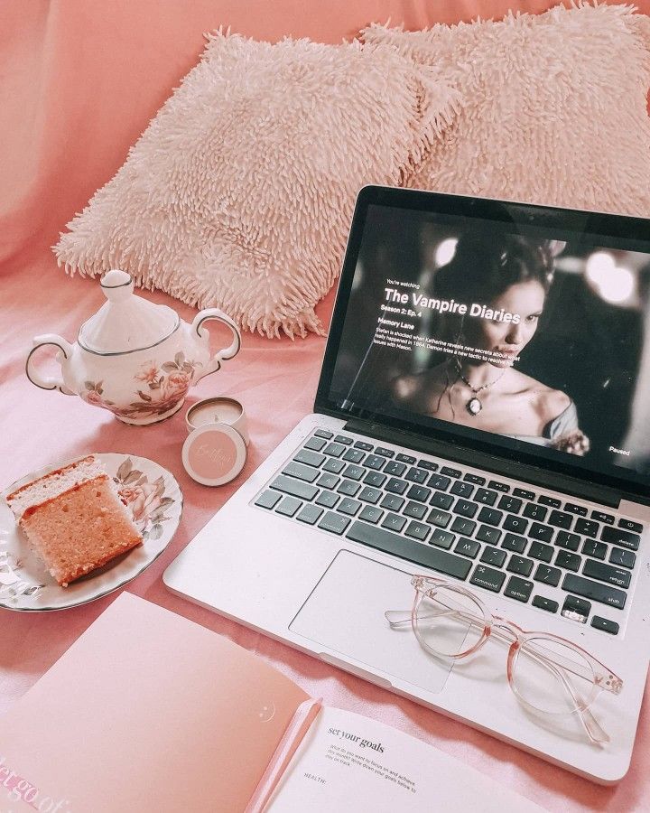 an open laptop computer sitting on top of a bed next to a slice of cake