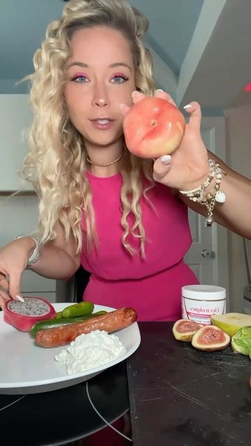 a woman in a pink dress is holding up a doughnut and pointing to the camera