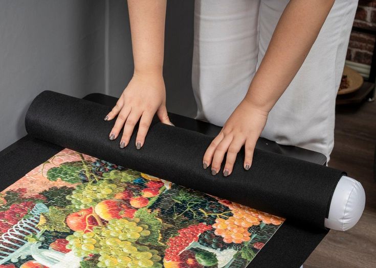 a woman rolling up a black mat on top of a table with grapes and oranges