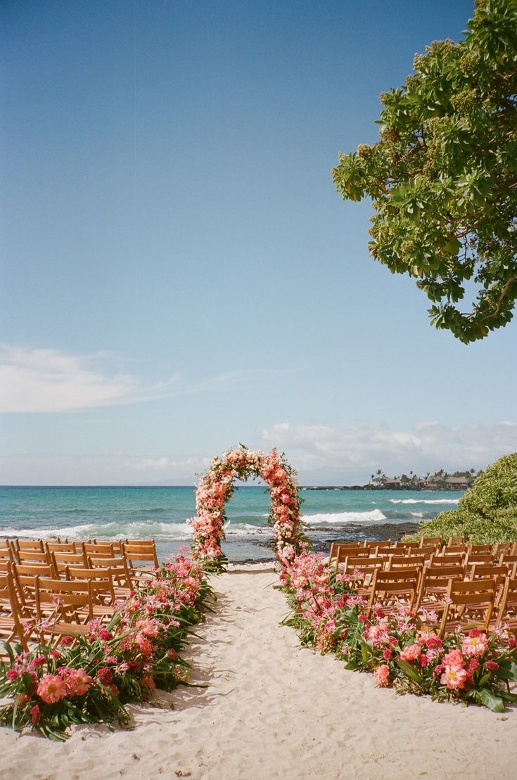 an outdoor ceremony set up on the beach with wooden chairs and flowers in the foreground