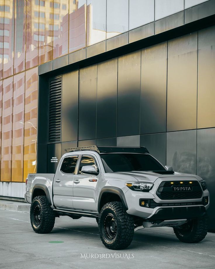 a silver toyota truck parked in front of a tall building next to a parking lot