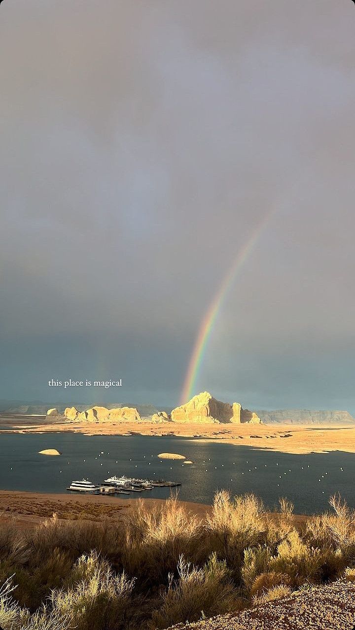 a rainbow in the sky over a body of water with mountains in the back ground