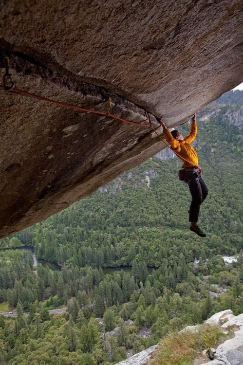 a man climbing up the side of a cliff with his hands in the air while holding onto ropes