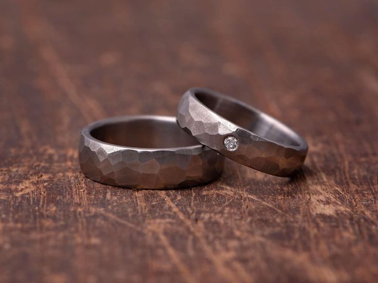 two wedding rings sitting on top of a wooden table with one diamond in the middle