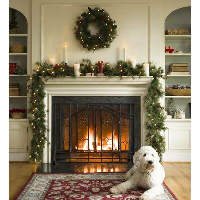 a white dog sitting in front of a fireplace with christmas decorations on the mantel