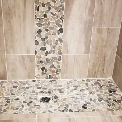 a walk in shower that has pebbles on the floor and tile around it, along with a toilet