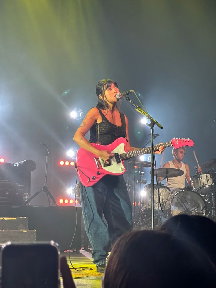 a woman standing on top of a stage holding a guitar