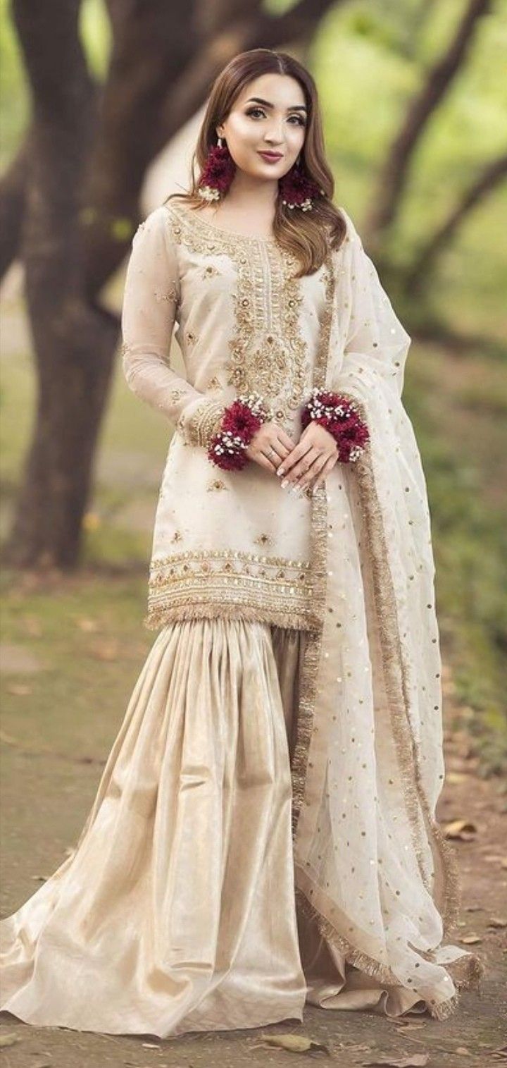 a woman in a white and beige outfit standing on a path with trees behind her