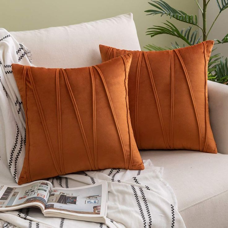 two orange pillows sitting on top of a white couch next to a potted plant