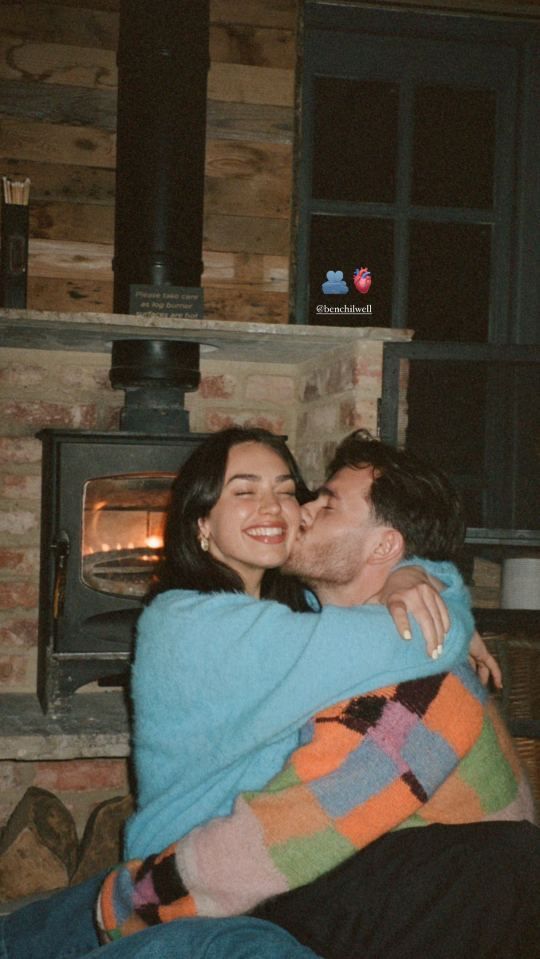 a man and woman sitting next to each other in front of a wood burning stove