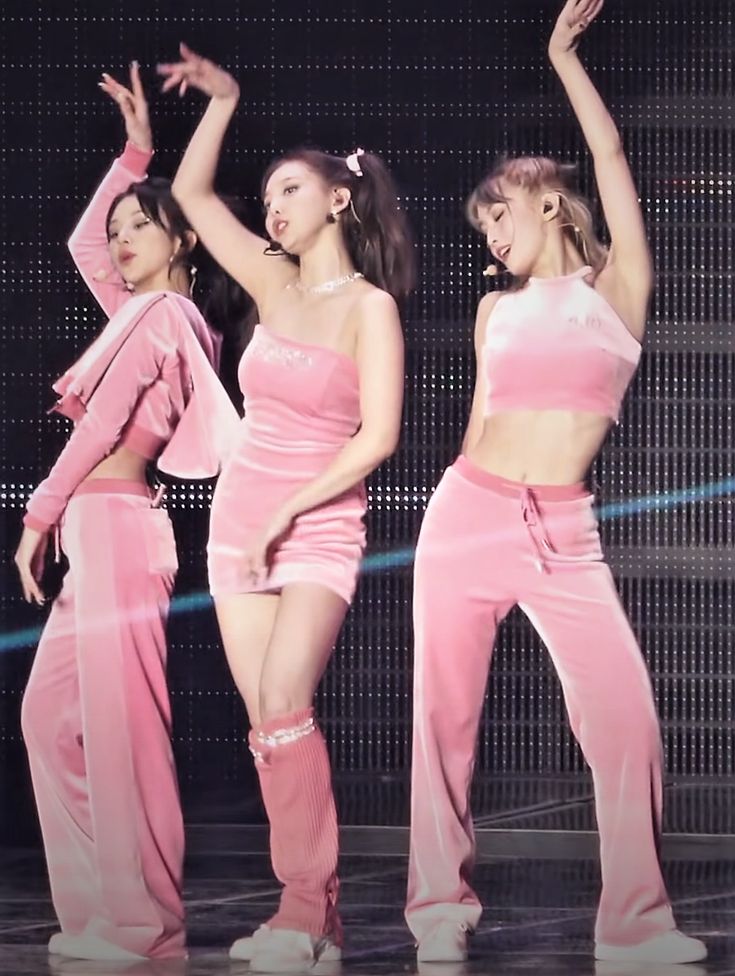 three girls in pink outfits on stage with one holding her arm up to the side