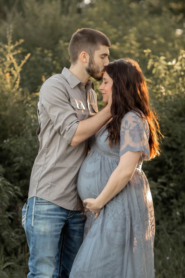 a pregnant couple cuddles in front of some bushes