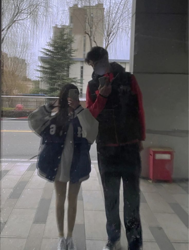 a man and woman walking down a sidewalk in the rain with their cell phones up to their ear