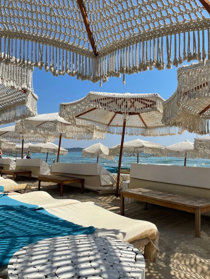 many white umbrellas and lounge chairs on the beach with blue water in the background