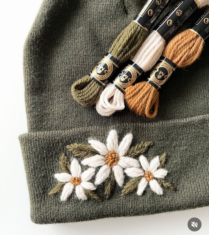 a knit hat with crochet flowers on it and knitting needles next to it