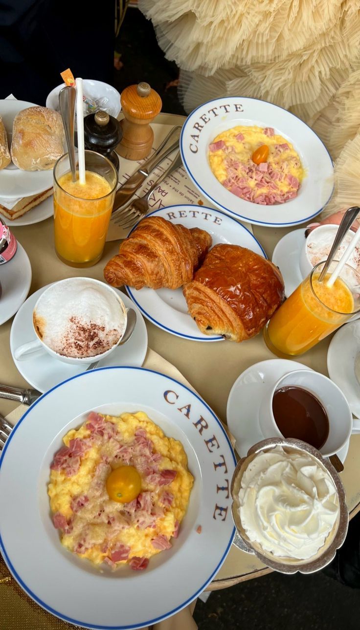 an assortment of breakfast foods on plates and in bowls, including croissants