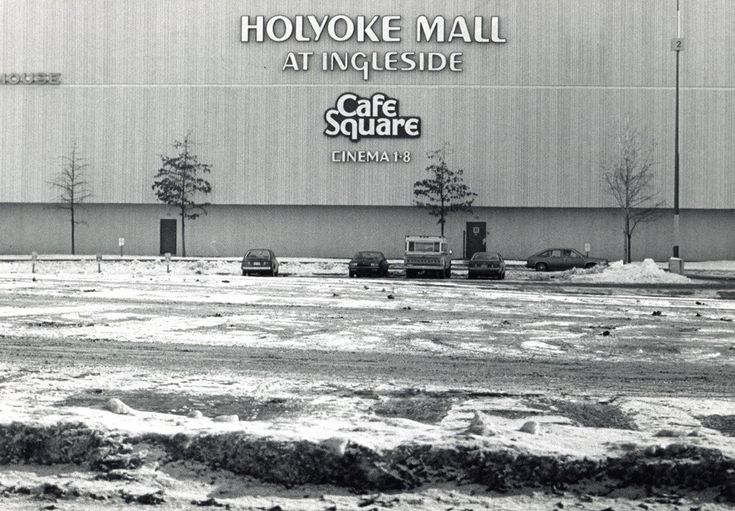 black and white photograph of an outside cafe square with cars parked in the parking lot