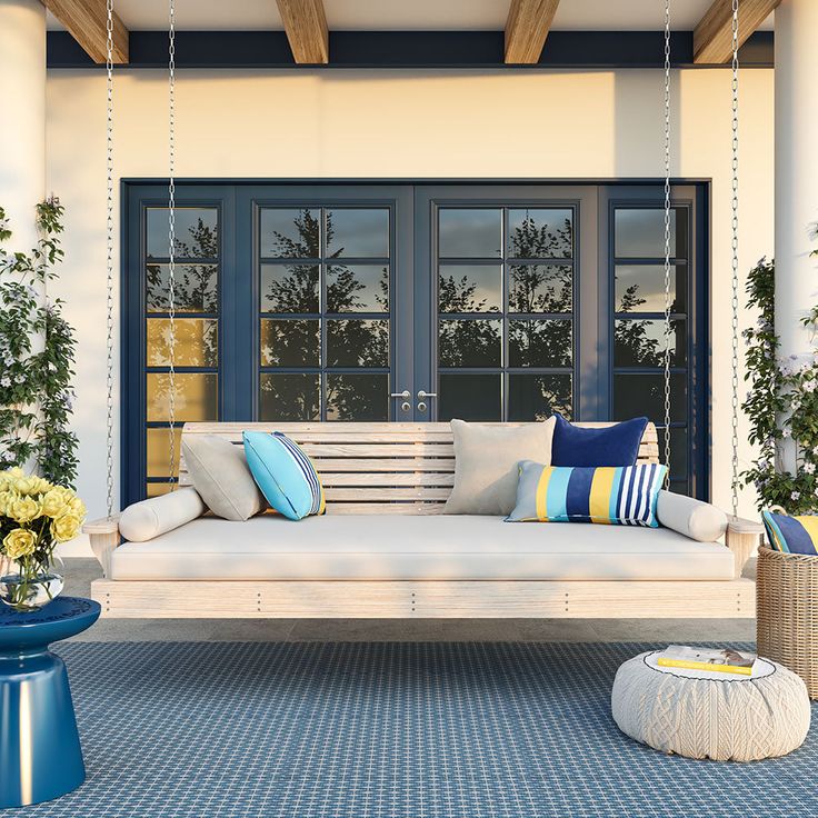 a white porch swing with blue and yellow pillows hanging from it's sides next to potted plants