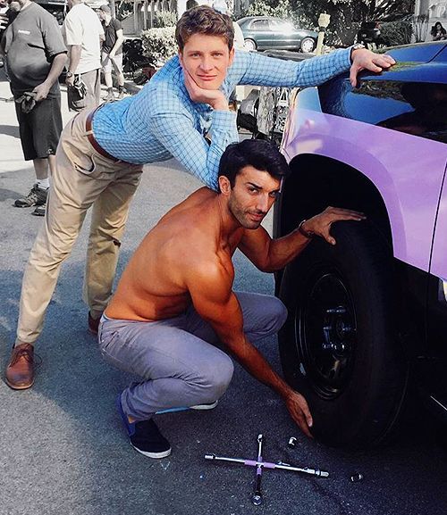 a man leaning on the hood of a purple car with another man standing next to it