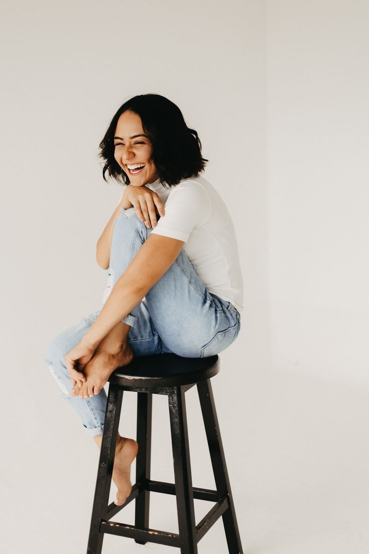 a woman sitting on top of a stool smiling at the camera with her legs crossed