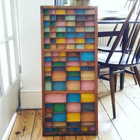 a multicolored wooden shelf sitting on top of a hard wood floor next to a chair