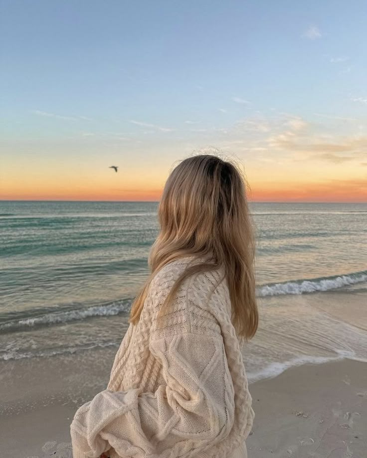 a woman standing on top of a sandy beach next to the ocean